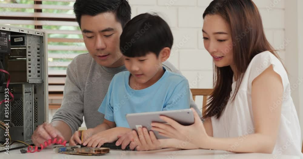 Young mother and father assist they son to assembling a computer at home. Mother open information in tablet to help little boy. Technology, Education, Family and Innovation concept.