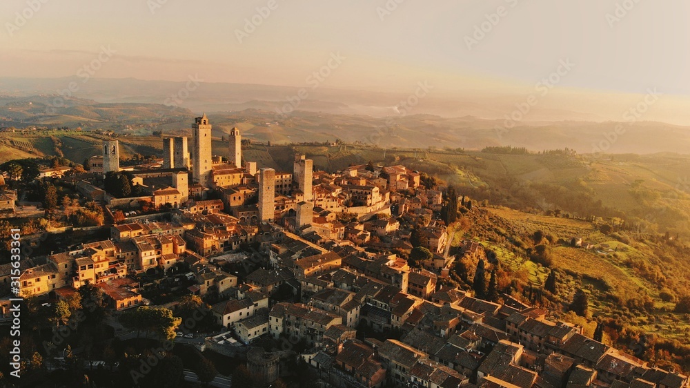 Aerial panorama view of San Gimignano taken on a drone at sunrise, one of the most famous cities in Tuscany, a picturesque region of Italy, the famous hills and cypresses, the fortress wall and towers