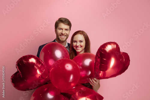 Happy holding balloons shaped hearts. Valentine's day celebration, happy caucasian couple on coral background. Concept of human emotions, facial expression, love, relations, romantic holidays. © master1305