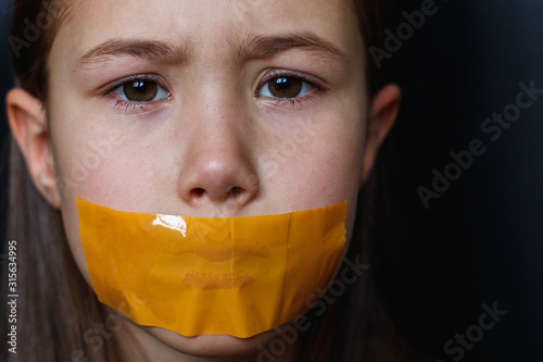 Unhappy girl with sticky tape over her mouth. Violation of human rights. Kidnapping. photo