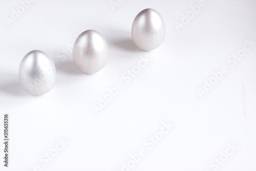 Easter holiday composition. Three silver colored eggs located in the upper left corner on a white background. Easter flat ley. Easter concept. Copyspace.