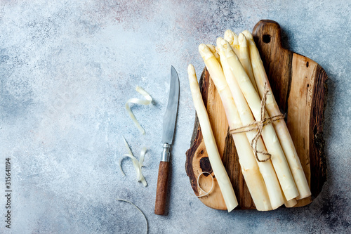 Bunch of raw white asparagus served on wooden board with knife. Top view, copy space