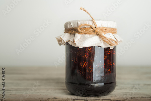 Traditional Trend Siberian dessert - young pine cones jam. Ukrainian cone jam in a jar on a light background close-up and copy space.