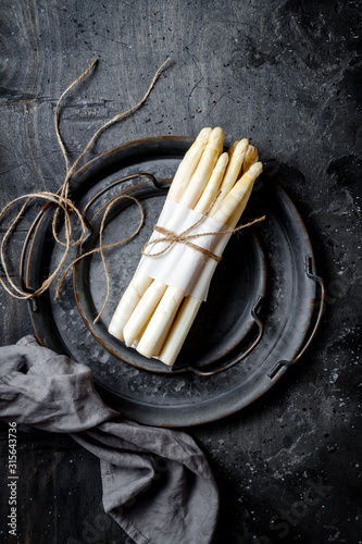 Bunch of fresh white asparagus on vintage metal tray over dark grey rustic background. Top view, copy space