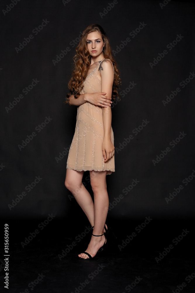 woman in beige dress on black background. Young sensual beautiful sexy woman posing in fashion beige dress naked on warm black background