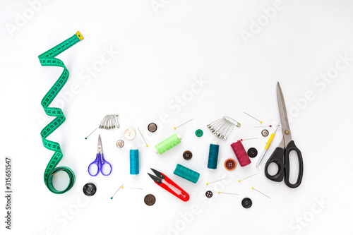 Sewing background. Set of tailoring tools on white background. Sewing accessories: scissors, threads, needles, pins, cloth, buttons, tape measure. Workplace of seamstress. Top view with copy space