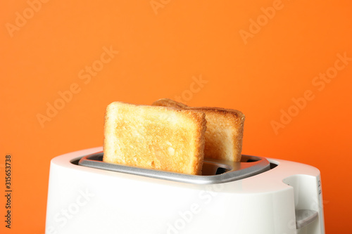 Toaster with bread on grey table against orange background, close up
