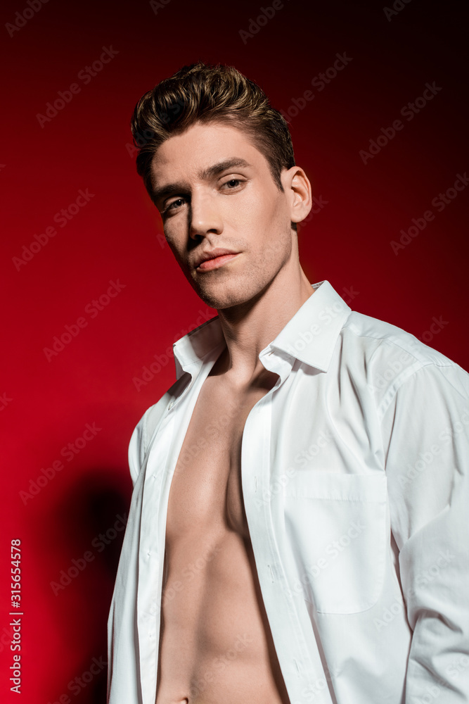Fototapeta premium sexy young elegant man in unbuttoned shirt with muscular bare torso on red background
