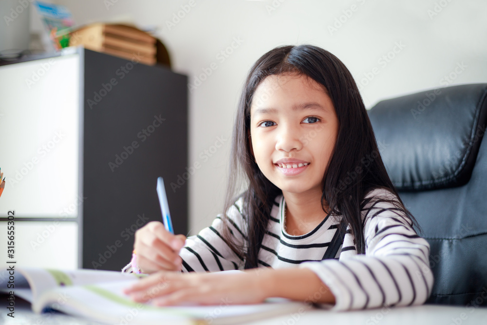 Smile little Asian girl doing homework with happiness for self learning and education concept select focus shallow depth of field Smile little Asian girl doing homework with happiness for self learning and education concept select focus shallow depth of field
