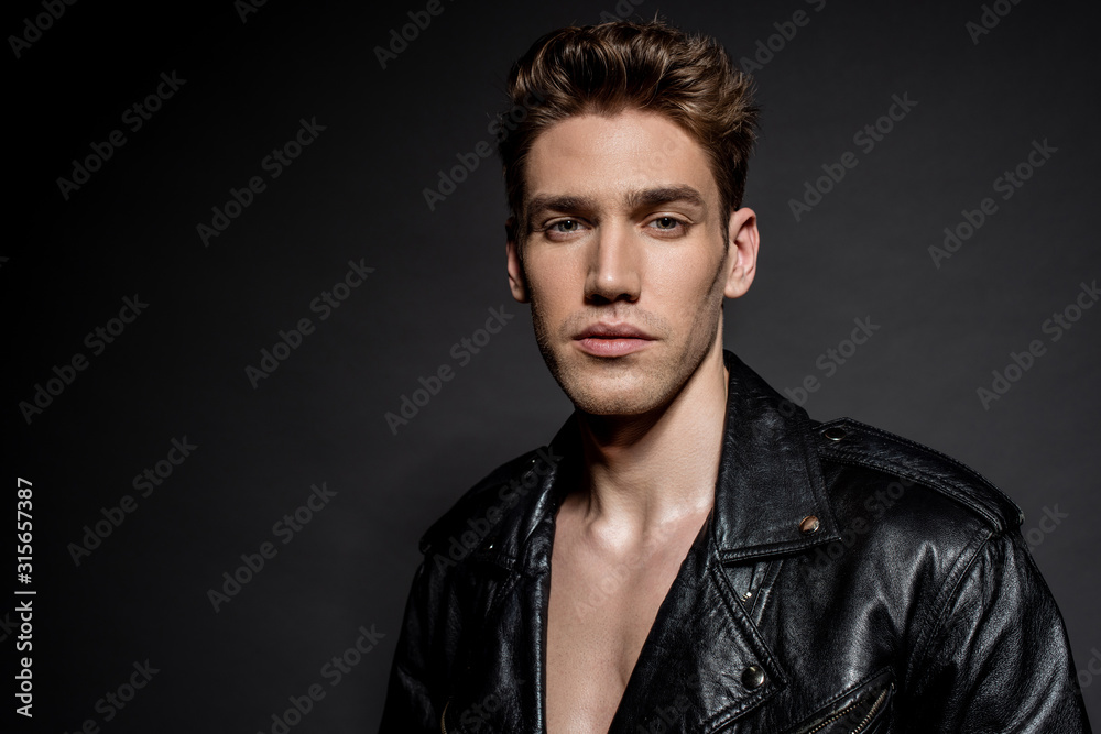 sexy young man in biker jacket on black background