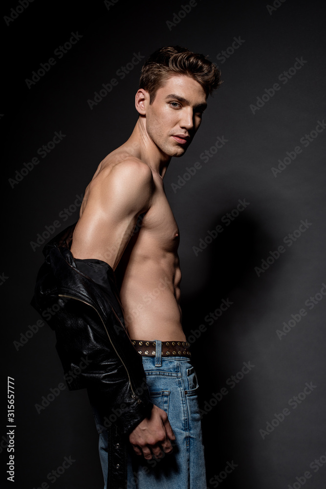 side view of sexy young man with muscular torso in biker jacket and jeans on black background side view of sexy young man with muscular torso in biker jacket and jeans on black background