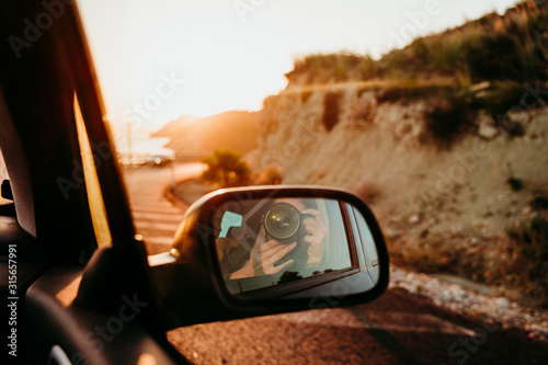 woman taking a self portrait in rear mirror in a car at sunset. travel concept