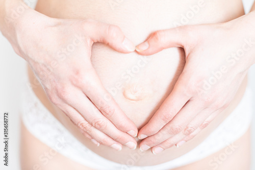 hands in the shape of a heart on a belly of a young pregnant woman