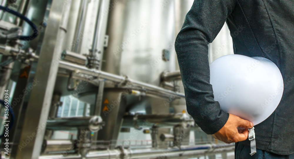 engineer suit white helmet for security stood on the details of shiny stainless steel pipes, tanks for the food industry. engineer suit white helmet for security stood on the details of shiny stainless steel pipes, tanks for the food industry.