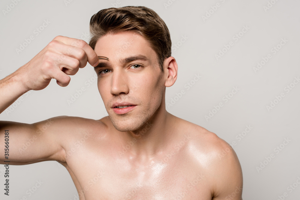 sexy man with bare torso pinching brows with tweezers isolated on grey sexy man with bare torso pinching brows with tweezers isolated on grey