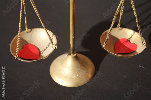 Two little paper red hearth in golden scale on black background. Vslentine day, love and justice, meserment of innocent