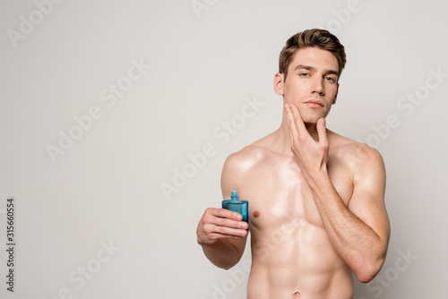 sexy man with muscular torso applying aftershave on face isolated on grey photo