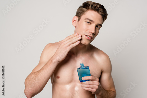 Konstfotografi sexy man with muscular torso applying after shave lotion isolated on grey