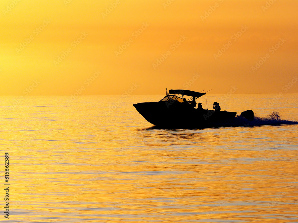 Silhouette of a power boat on the Gulf of Mexico in front of an orange sunset.