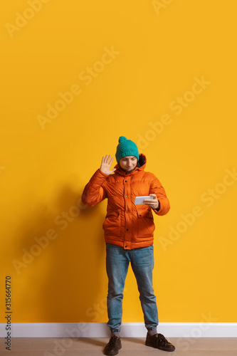 Using gadgets anywhere. Young caucasian man using smartphone, serfing, chatting, betting. Full length portrait isolated on yellow background. Concept of modern technologies, millennials, social media.
