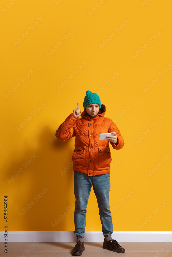 Pointing up. Young caucasian man using smartphone, serfing, chatting, betting. Full length portrait isolated on yellow background. Concept of modern technologies, millennials, social media.