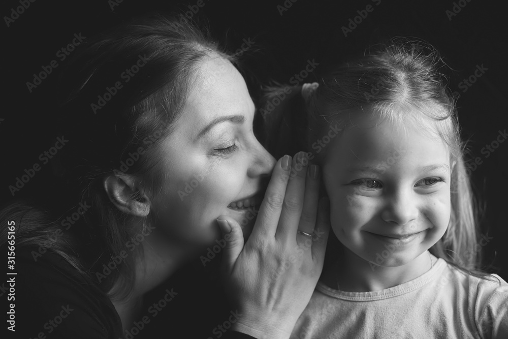 black-and-white portrait of a mother with a little daughter, a woman whispers a secret on a spit, family relations black-and-white portrait of a mother with a little daughter, a woman whispers a secret on a spit, family relations