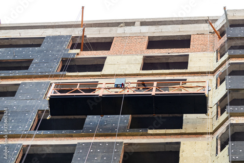 Wall Mural Suspended construction craddle near wall of hightower residentaial building with insulation and ventilated facade on construction site