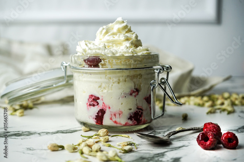 Whipped cream with fresh raspberries in a glass jar on a white marble background