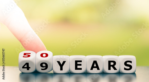 Symbol for turning 50 years old. Hand turns a dice and changes the expression "49 years" to "50 years".