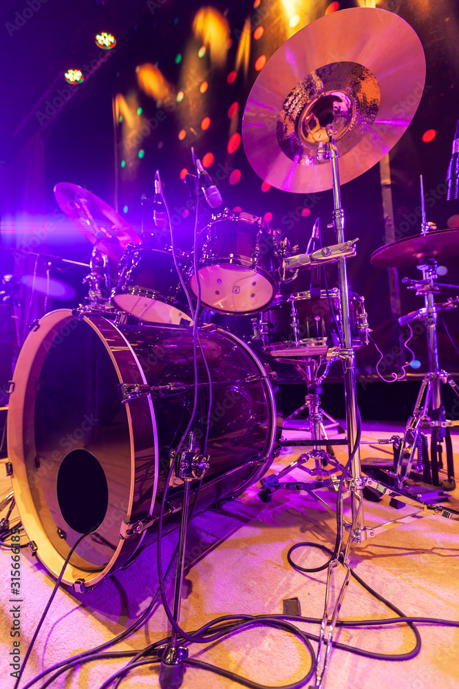 Drum set with bass drum, tom-toms, cymbals and microphones on the stage with violet-red illumination Drum set with bass drum, tom-toms, cymbals and microphones on the stage with violet-red illumination