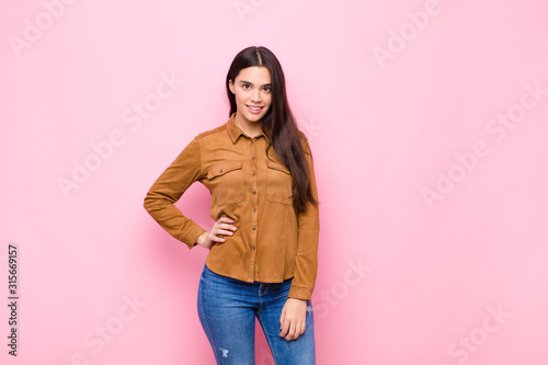 Foto young pretty woman smiling happily with a hand on hip and confident, positive, p