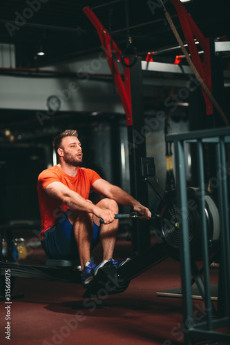 Young Muscular Fit Man using Rowing Machine at Gym