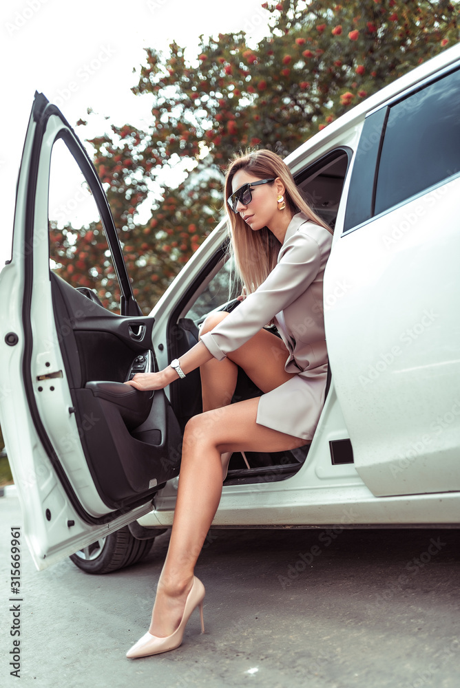Beautiful girl gets out of white business car sedan. In summer in city in  parking lot.