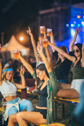 Female friends sitting and cheering with beer at the music festival