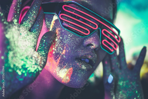 Beautiful young woman dancing and making party with fluorescent painting on her face. Neon facial portraits photo