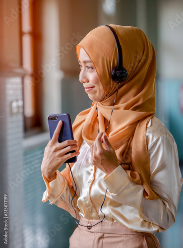 Happy young muslim woman wearing Hijap  listening to the music from her mobile phone, looking through the window and smiling. photo