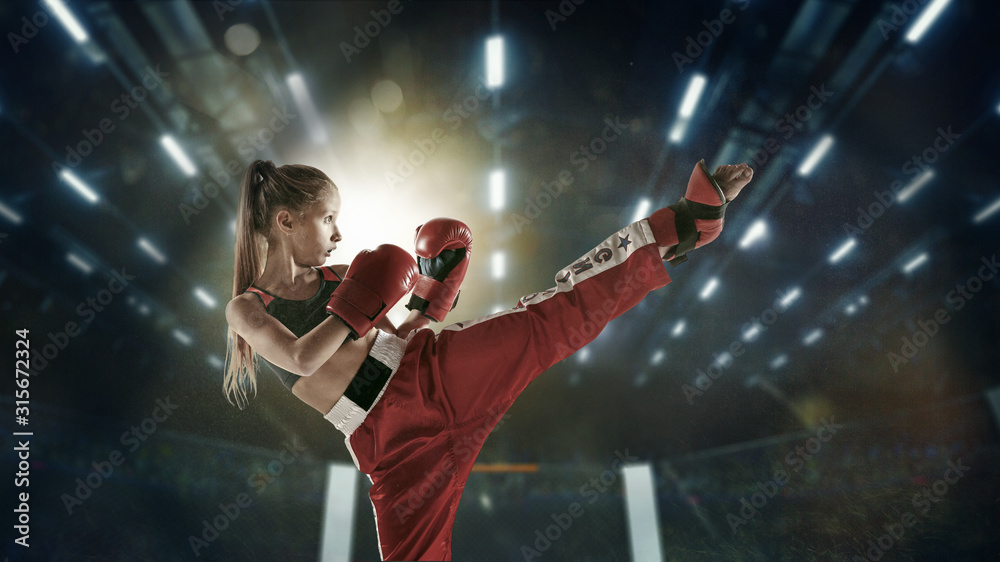 Confident. Young female kickboxing fighter training in the gym. Caucasian blonde girl in red sportswear practicing in martial arts. Concept of sport, healthy lifestyle, motion, action, youth.