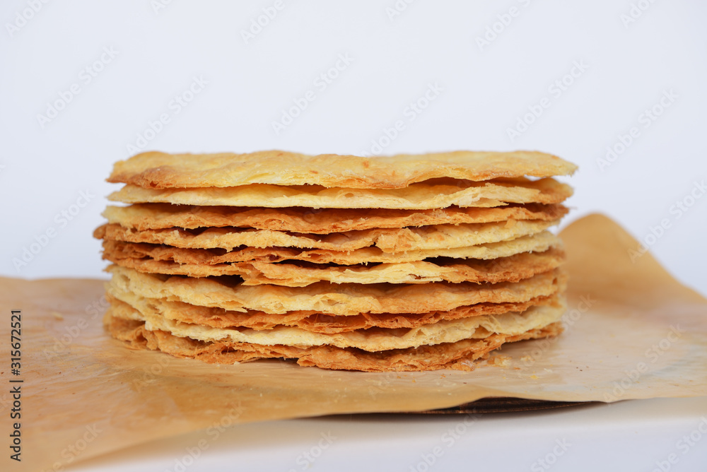 Tasty crispy baked round puff pastry layers of homemade traditional Russian napoleon cake on parchment on white background