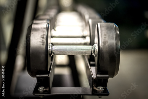 Dumbbell weight, equipment for workout, there are available on row rack in fitness gym. Selected focus on metal handle.