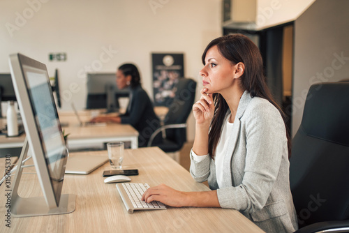 Serious businesswoman working on computer in co-working office.
