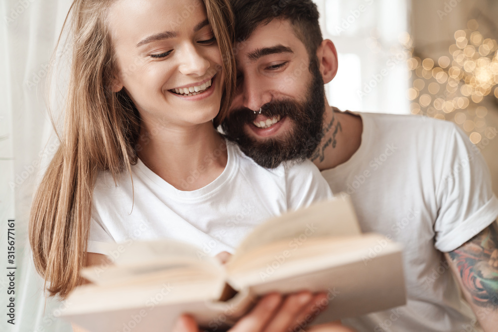 Image of happy young couple laughing and reading book while sitting Image of happy young couple laughing and reading book while sitting