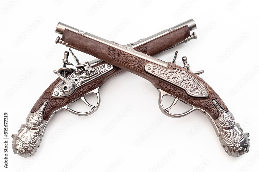 Firearms dating to the american revolution and antique collectables concept with ornate old fashioned dueling flintlock pistols crossed in duel isolated on white background with clipping path cutout