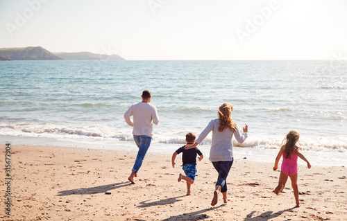 Rear View Of Family On Beach Running Across Sand Towards Sea