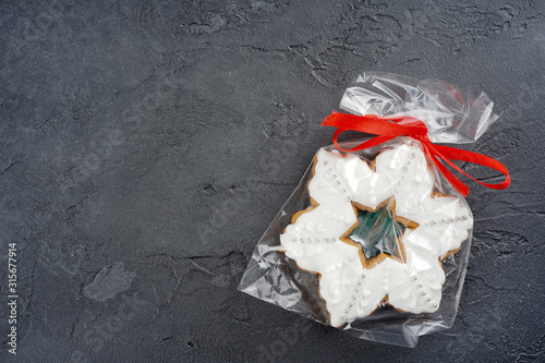 Snowflake shape gingerbread cookie in package, red ribbon on gray concrete background. Cooking, recipe, card, Christmas concept. Top view, flat lay, copy space