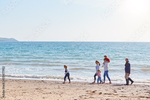 Multi-Generation Family Walking Along Shoreline Of Beach By Waves Together