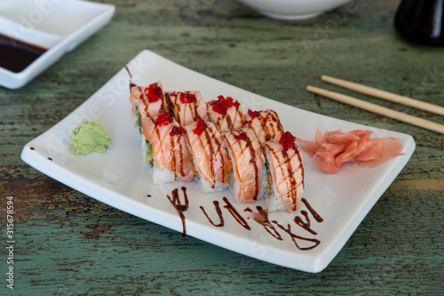 Flambemon Salmon Uramaki dish stuffed with avocado with ginger and wasabi on vintage wooden background