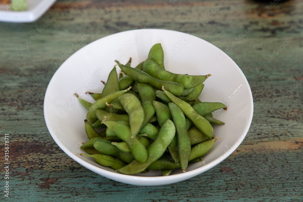 Bowl of Edamame, green beans of boiled soybeans on wooden background. Japanese food. Bowl of Edamame, green beans of boiled soybeans on wooden background. Japanese food.