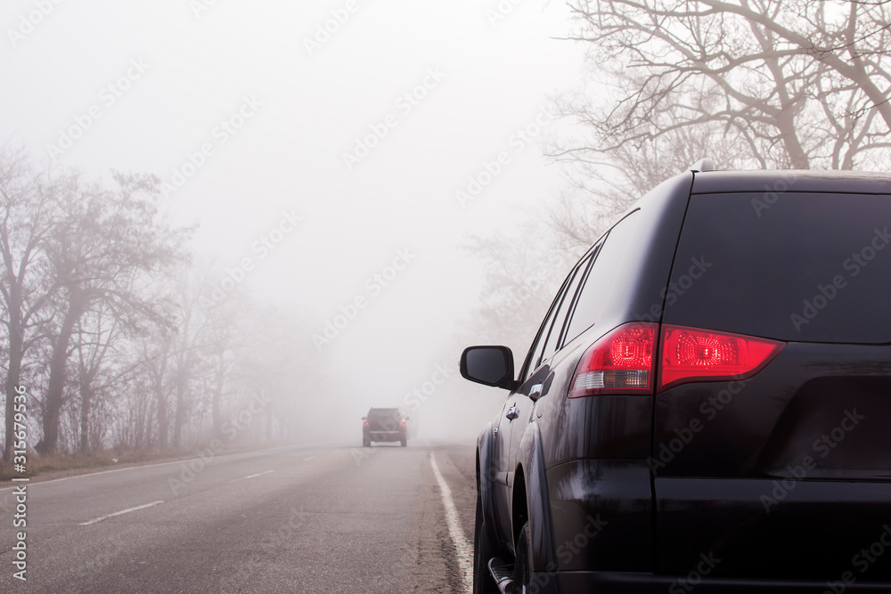 Cars on the road in the fog. Bad winter weather and dangerous automobile traffic on the road. Light vehicles in fog. Foggy gray road, cars driving fading into the fog. Space for text.