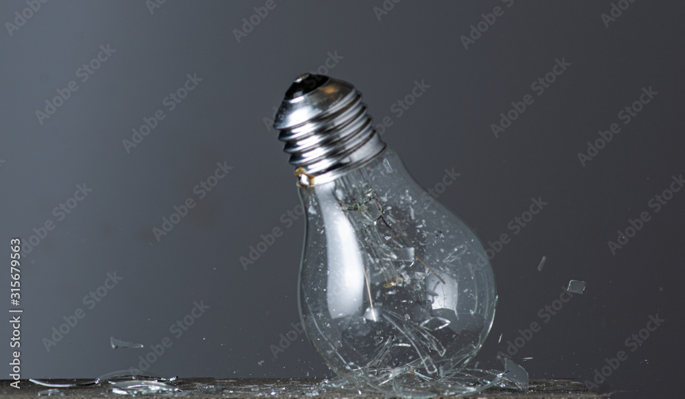 a falling round incandescent lamp is broken into fragments on a stone on a gray background