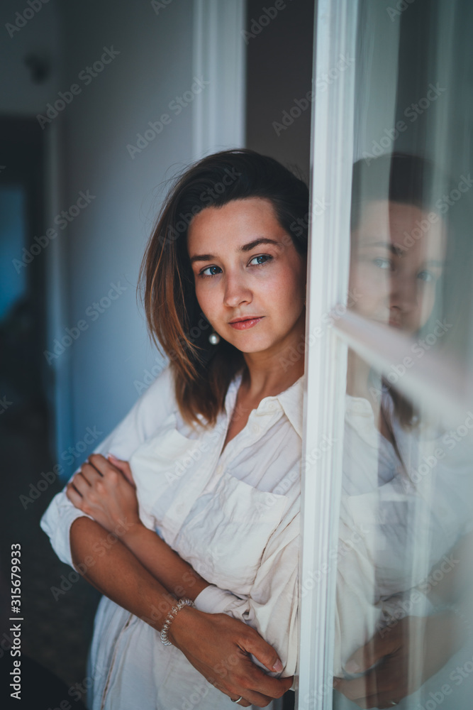 Closeup Portrait of Young Smiling Female Manager or Creative Artist standing near the Window with Crossed Hands Looks  Thoughtful